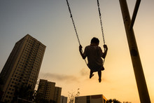 Child Swinging On Swing In Sunset In City With Building On Background