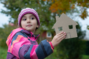 The girl is five years old. She is holding a house cut out of cardboard.