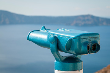 Wall Mural - Bright sunny close-up of blue binoculars pointed from a lookout over the dramatic Mediterranean caldera of Santorini, Greece