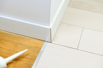 Poor joint of the corner of a white plinth on the floor of ceramic tiles and parquet.