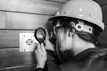 selective focus on construction inspector woman's hand holding a magnifying glass to looking closely at 220v electricity outlet for clothes dryer