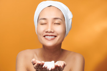 Wall Mural - Young Asian woman showing foaming cleanser on her hand while wearing a bath towel over orange background.