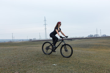 Girl on a mountain bike on offroad, beautiful portrait of a cyclist at sunset, Fitness girl rides a modern carbon fiber mountain bike in sportswear. Close-up portrait of a girl in a helmet and glasses