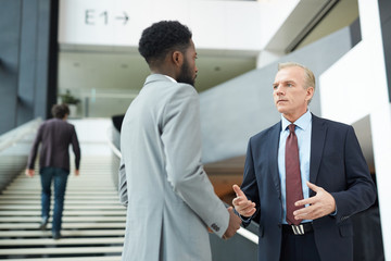 horizontal low angle shot of two modern businessmen standing in front of each other discussing somet