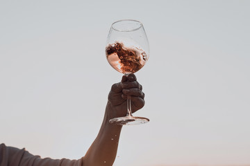 Wall Mural - Glass of wine with splashes in woman's hand against the sunset sky.