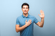 handsome young man with neutral smile in blue polo shirt with hand on chest giving oath against blue background. studio shoot