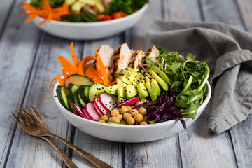 A close up of a buddha bowl filled with various vegetables, chick peas and grilled chicken.