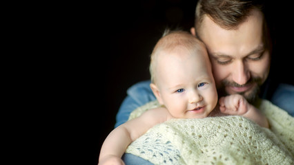 A happy father lives in the arms of a newborn baby, hugs and poses creamly. Paternity