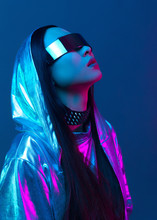 Neon Portrait Of A Girl Of Asian Appearance, Dressed In Futuristic Clothes And Glasses. Neon Blue And Pink Light. Virtual Reality Glasses