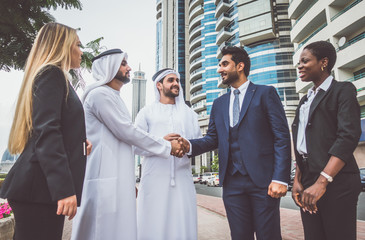Wall Mural - Mixed business team in Dubai. Business meeting with men wearing kandura and western people walking on the street