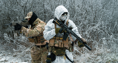 Wall Mural - Two men in camouflage white, green uniform with machineguns back to back. Soldiers with muchinegun in the winter forest. Horizontal photo, side view.