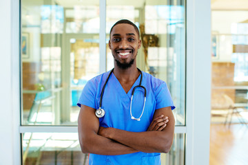 portrait of a friendly male doctor or nurse wearing blue scrubs uniform and stethoscope, with arms c