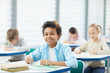 © AnnaStills - Horizontal medium close up portrait of happy mixed-race boy with kinky hair sitting at school desk looking at camera smiling, copy space