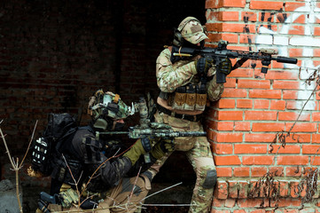 Wall Mural - Two men in camouflage cloth and black uniform with machineguns. Soldiers with muchinegun aims aiming standing beside wall.