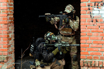 Wall Mural - Two men in camouflage cloth green and black uniform with machineguns. Soldiers with muchinegun aims aiming in oposite sides, standing beside wall.