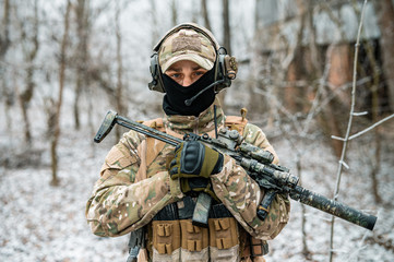 Wall Mural - Man in camouflage uniform hold machinegun. Soldier in the winter forest. Horizontal photo side view.