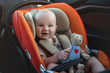 Smilimg baby boy with a bear toy sitting in the car seat.