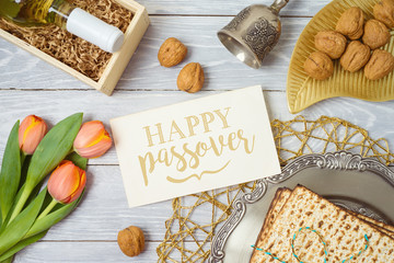 Jewish holiday Passover greeting card with matzo, seder plate, wine and tulip flowers on wooden table.