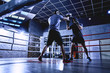 Professional boxers with gloves train fights in indoor boxing ring, dark colors