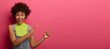 © WHstudio Leushin N - Best offer for you. Positive dark skinned woman points index fingers at copy space, has toothy smile, wears denim overalls, gestures against pink background, says best shopping here. Check it out