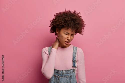 Cuadros en Lienzo Displeased young African American woman feels discomfort in spine, touches neck