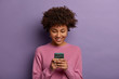 © wayhome.studio  - Pretty curly woman holds modern mobile phone, types messages on smartphone device, enjoys online communication, downloads special app for chatting, smiles tenderly, isolated on purple studio wall