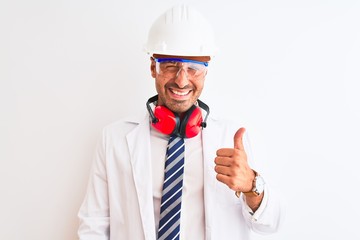 Wall Mural - Young chemist man wearing security helmet and headphones over isolated background doing happy thumbs up gesture with hand. Approving expression looking at the camera with showing success.