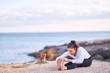 © Krakenimages.com - Young beautiful sportwoman smiling happy practicing yoga. Coach with smile on face teaching seated forward fold pose at the beach