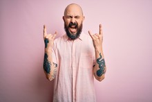 Handsome Bald Man With Beard And Tattoo Wearing Casual Shirt Over Isolated Pink Background Shouting With Crazy Expression Doing Rock Symbol With Hands Up. Music Star. Heavy Concept.