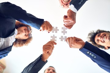 Group of business workers smiling happy and confident. Standing on a circle with smile on face trying to connect puzzle pieces at the office.