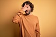 © Krakenimages.com - Young handsome man with beard wearing casual sweater standing over yellow background peeking in shock covering face and eyes with hand, looking through fingers with embarrassed expression.
