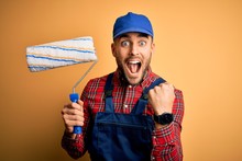 Young Handsome Painter Man Painting Wall Using Roller Over Isolated Yellow Background Screaming Proud And Celebrating Victory And Success Very Excited, Cheering Emotion