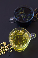 butterfly pea tea and Jasmine tea. two cups of hot tea with dry flowers on a black table top view. Healthy lifestyle. glass cups of blue and yellow herbal tea on a black background. Hot drinks.