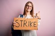 © Krakenimages.com - Young beautiful redhead activist woman holding banner with strike message happy with big smile doing ok sign, thumb up with fingers, excellent sign