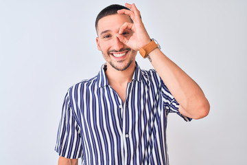 Poster - Young handsome man wearing nautical striped shirt standing over isolated background doing ok gesture with hand smiling, eye looking through fingers with happy face.