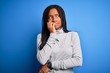 © Krakenimages.com - Young african american woman standing wearing casual turtleneck over blue isolated background looking stressed and nervous with hands on mouth biting nails. Anxiety problem.