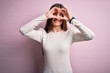 © Krakenimages.com - Young beautiful woman with blue eyes wearing casual white t-shirt over pink background Doing heart shape with hand and fingers smiling looking through sign