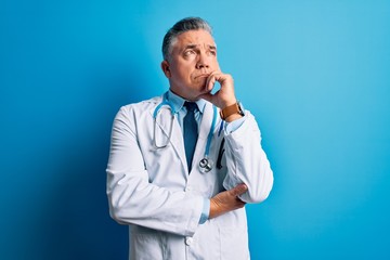 Canvas Print - Middle age handsome grey-haired doctor man wearing coat and blue stethoscope with hand on chin thinking about question, pensive expression. Smiling and thoughtful face. Doubt concept.