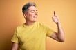 © Krakenimages.com - Young handsome modern man wearing yellow shirt over yellow isolated background Looking proud, smiling doing thumbs up gesture to the side
