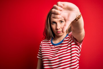 Poster - Young beautiful blonde woman wearing casual striped t-shirt over isolated red background looking unhappy and angry showing rejection and negative with thumbs down gesture. Bad expression.