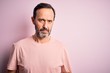 © Krakenimages.com - Middle age hoary man wearing casual t-shirt standing over isolated pink background skeptic and nervous, frowning upset because of problem. Negative person.