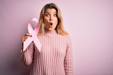 Poster - Young beautiful blonde woman asking for support cancer holding pink ribbon symbol scared in shock with a surprise face, afraid and excited with fear expression