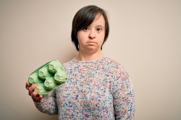 Sticker - Young down syndrome woman holding cardboard egg cup from fresh healthy eggs with a confident expression on smart face thinking serious