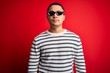 © Krakenimages.com - Young brazilian man wearing funny thug life sunglasses over isolated red background with serious expression on face. Simple and natural looking at the camera.