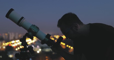 Wall Mural - astronomer with a telescope watching at the stars and moon with blurred city lights in the backgroun