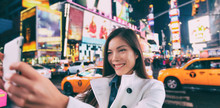 New York City Tourist Selfie Asian Happy Woman Taking Photo At Night In Times Square, Manhattan, USA. Girl Traveler Joyful And Smiling. Multiethnic In Her 20s.