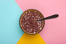 Chocolate cereal balls with milk in bowl on colored background. Concept for a healthy diet. Top view
