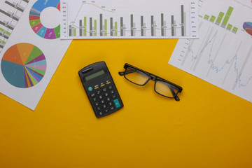 Wall Mural - Classic eyeglasses, calculator with graphs and charts on yellow background. Economic calculation, analytics, business concept. Top view. Top view