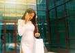 © splitov27 - Young afro woman in white dress with paper shopping bags talking on the phone outdoors against the background of a business building
