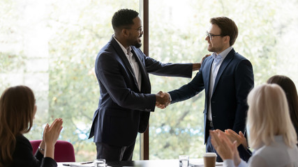 Wall Mural - Confident young african American businessman shake hand greeting get acquainted with excited male colleague at meeting, smiling biracial man boss shake hand of coworker congratulate with job promotion